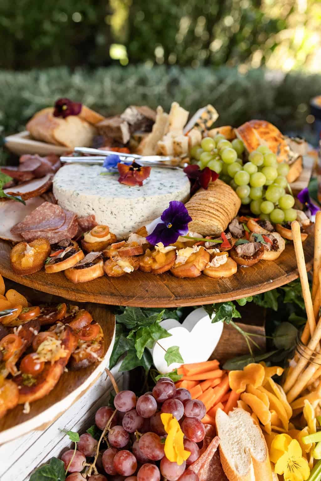 A platter of cheese, fruit, and meats on a wooden board.